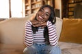 Portrait of young African American woman leaning on her hands and smiling, looking at camera, sitting on couch at home Royalty Free Stock Photo