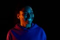 Portrait of young african american woman posing and smiling isolated on dark background in multicolored neon light Royalty Free Stock Photo