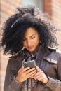 Portrait of young African American woman texting on her smartphone. Brunette with curly hair in leather jacket and Royalty Free Stock Photo