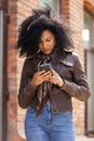 Portrait of young African American woman texting on her smartphone. Brunette with curly hair in leather jacket and Royalty Free Stock Photo