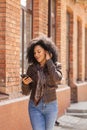 Portrait of young African American woman texting on her smartphone and smiling. Brunette with curly hair in leather Royalty Free Stock Photo