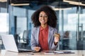Portrait of a young African American woman working in an office, sitting at a desk with a laptop, holding phone and Royalty Free Stock Photo