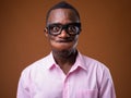 Portrait of young African businessman making faces against brown background