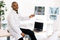 Portrait Of young African Male doctor Obstetrician, surgeon In Hospital, sitting on the table with laptop and holding Royalty Free Stock Photo