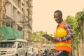 Young happy black African man construction worker smiling while reading on clipboard and holding hard hat at building Royalty Free Stock Photo