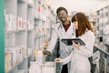 Portrait of young African man pharmacist technician standing with female Caucasian colleague in modern drugstore Royalty Free Stock Photo