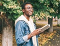 Portrait young african man student with a book looking away wearing an eyeglasses in autumn city park Royalty Free Stock Photo