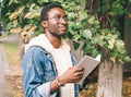 Portrait young african man student with a book looking away wearing an eyeglasses in autumn city park Royalty Free Stock Photo