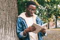 Portrait young african man student reading a book wearing an eyeglasses in autumn city park Royalty Free Stock Photo