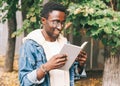 Portrait young african man student reading a book wearing an eyeglasses in autumn city park Royalty Free Stock Photo