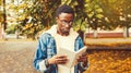 Portrait of young african man student reading a book wearing eyeglasses in autumn city park Royalty Free Stock Photo