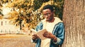 Portrait of young african man student reading a book wearing eyeglasses in autumn city park Royalty Free Stock Photo