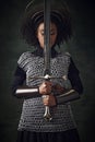 Portrait of young African woman, medieval warrior in chainmail armor with halo-like rings above head holding sword close Royalty Free Stock Photo