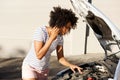 Young african woman standing by broken down car parked on the road and calling for assistance Royalty Free Stock Photo