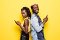 Portrait of a young afro american couple standing back to back using mobile phones isolated over yellow background Royalty Free Stock Photo