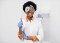 Portrait of young afro american lady otolaryngologist with a medical mirror on her head, smiling and looking at the