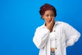 Portrait of young afro woman with bored face expresison touching her chin against blue background Royalty Free Stock Photo