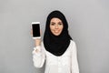 Portrait of young arab woman 20s in islamic headscarf with oriental makeup demonstrating black screen of cell phone at camera, is Royalty Free Stock Photo