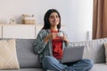 Portrait of young Arab woman working on laptop pc, sitting on couch and drinking coffee at home office, copy space Royalty Free Stock Photo