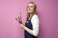 Portrait of young artist, girl holds brushes and smiles on a pink background, student of art school, profession of an artist