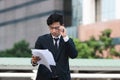 Portrait young Asian business man in suit analyzing charts or paperwork in hands outdoors