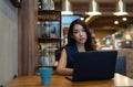 Portrait of young Asian business woman on a coffee break. Her using laptop while sitting at cafe and looking at camera. Freelance Royalty Free Stock Photo