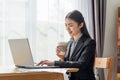 Young Asian business woman drinking coffee and using her laptop in her office Royalty Free Stock Photo