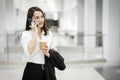 Portrait of a young Asian business woman talking over cellphone and holding cup of coffee in business building. Photo of beautiful Royalty Free Stock Photo