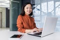 Portrait of a young Asian business woman working in the office at the laptop, smiling at the camera Royalty Free Stock Photo