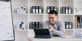 Portrait of a young Asian businessman smiling while using a laptop and writing down notes while sitting at his desk in a Royalty Free Stock Photo