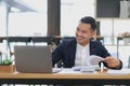 Portrait of a young Asian businessman smiling while using a laptop and writing down notes while sitting at his desk in a Royalty Free Stock Photo