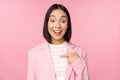 Portrait of young asian businesswoman with surprised, excited face expression, pointing finger at herself, standing in Royalty Free Stock Photo