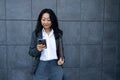 Portrait of Asian businesswoman using mobile phone while standing against wall outdoors Royalty Free Stock Photo