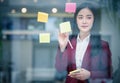 Portrait of Young asian businesswoman writing sticky paper pad on glass in modern office. Business plan concept Royalty Free Stock Photo