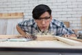 Portrait of young asian carpenter wearing safety glasses blowing sawdust after polishing with sanding machine Royalty Free Stock Photo