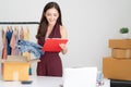 Portrait of young Asian casual woman working small business online packing jeans to cardboard box and check order in home office.