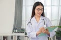 Portrait of a young Asian female doctor wearing glasses Standing with a clipboard in her office at the clinic Royalty Free Stock Photo
