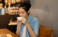 Portrait of young Asian gorgeous female with her eyes closed enjoying the smell of fresh delicious coffee at coffee shop
