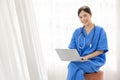 Portrait of a young Asian happy nurse wearing medical scrubs looking at the camera with a stethoscope and using a laptop. Royalty Free Stock Photo