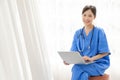 Portrait of a young Asian happy nurse wearing medical scrubs looking at the camera with a stethoscope and using a laptop. Royalty Free Stock Photo
