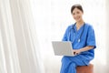 Portrait of a young Asian happy nurse wearing medical scrubs looking at the camera with a stethoscope and using a laptop. Royalty Free Stock Photo