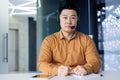 Portrait of a young Asian male businessman sitting at a desk in an office wearing a headset and looking seriously at the Royalty Free Stock Photo