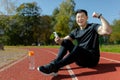 Portrait of a young Asian man, an athlete sitting on a treadmill with a phone. He is happy, looks into the camera. Shows Royalty Free Stock Photo