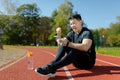 Portrait of a young Asian man, an athlete sitting on a treadmill with a phone. Rejoicing, showing a victory gesture, yes Royalty Free Stock Photo