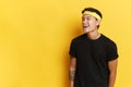 Portrait of young Asian man in black T-shirt posing on studio yellow background, stands on the right and winks Royalty Free Stock Photo