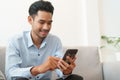 Portrait of young asian man handsome wearing blue shirt is reading using smartphone and sitting on sofa in living room at home Royalty Free Stock Photo