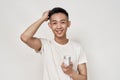 Portrait of young asian man with problematic skin and hyperpigmentation on his face smiling at camera, holding cream jar