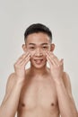 Portrait of young asian man with problematic skin and hyperpigmentation smiling at camera, applying cream on his face