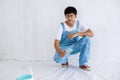 Portrait young asian man in white shirt with bear suit sit and painted plot on hand and look at camera in white wall, renovation