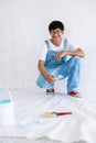 Portrait young asian man in white shirt with bear suit sit and painted plot on hand and look at camera in white wall, renovation